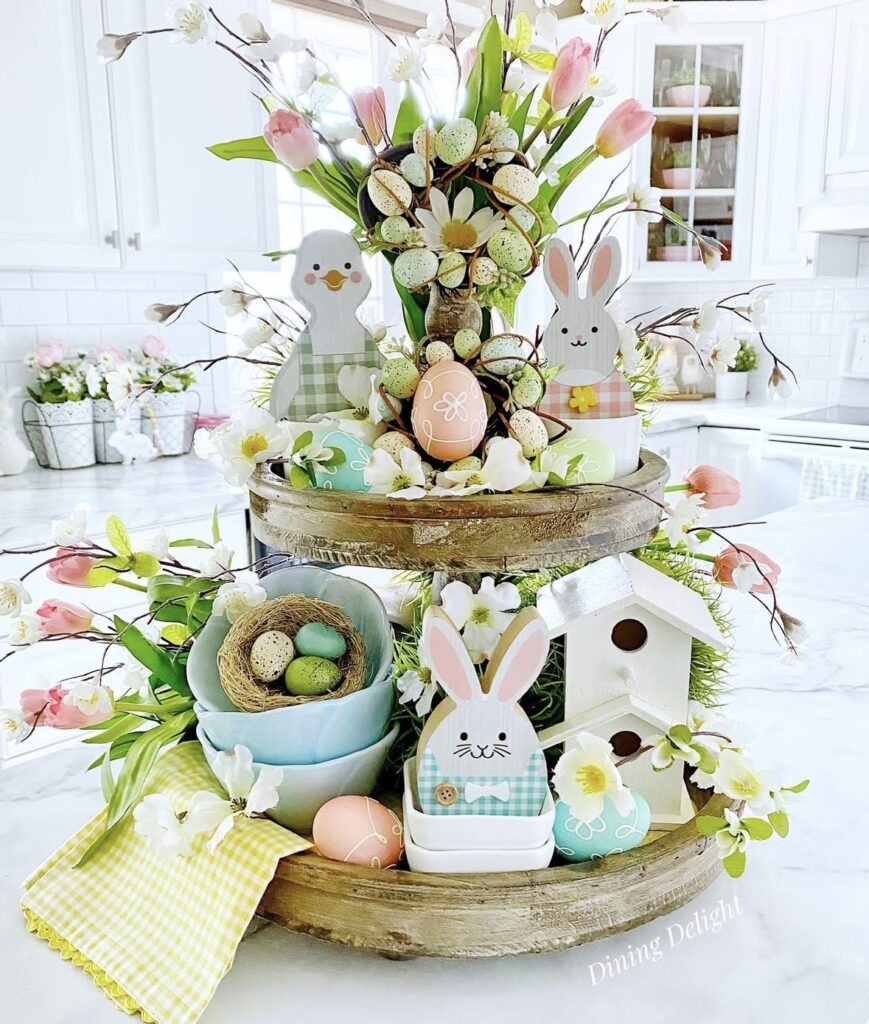 Pastel spring Easter tiered tray decor with pink tulips, speckled eggs, cute chick and bunny, small birdhouse, and bowls with nest eggs.