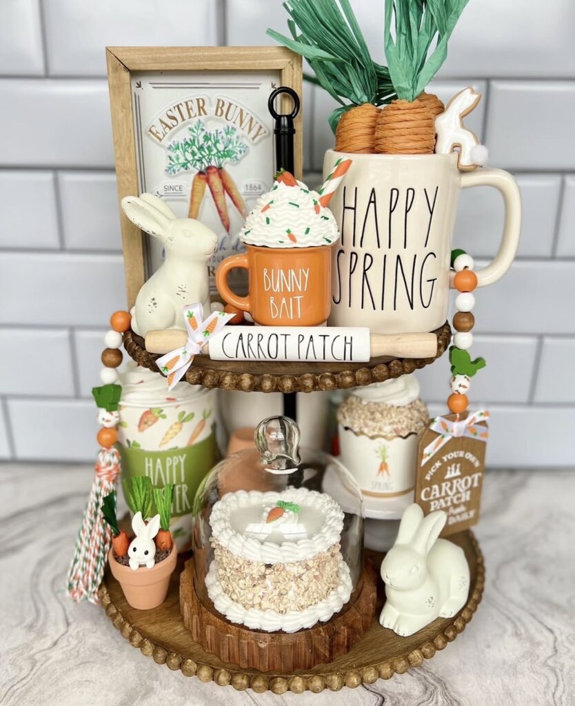 Carrot patch Easter tiered tray with “Happy Spring” mug, “Bunny Bait” cup, faux carrots, bunny figurines, and a mini cake under a glass cloche.