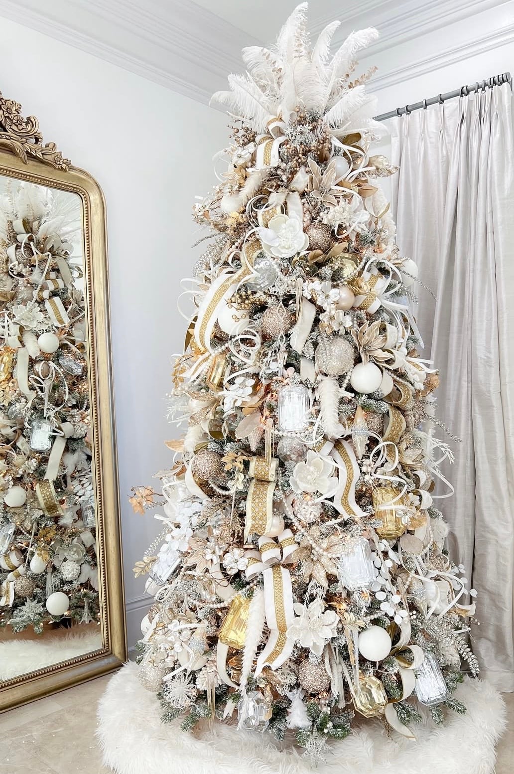 White and gold Christmas tree with white feather topper and with natural greenery, ribbon, and rustic accents.