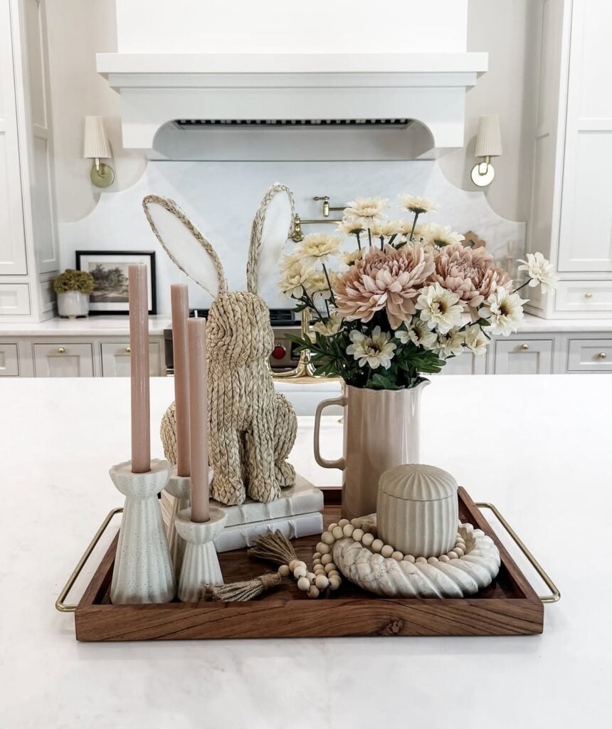 Elegant Easter kitchen island tray with blush flowers, woven bunny decor, pink taper candles, bead garland, and a neutral ceramic jar.