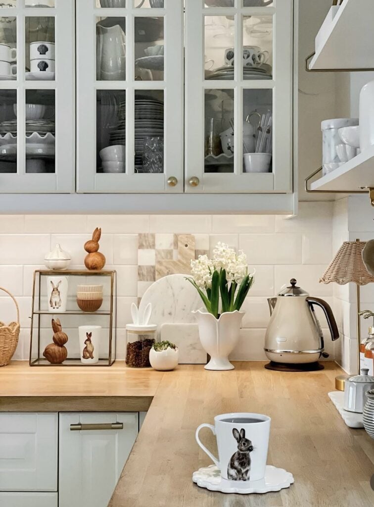 Neutral Easter kitchen counter decor with white hyacinths in a tulip vase, wooden bunny accents, a bunny mug, and soft cream styling on butcher block counters.