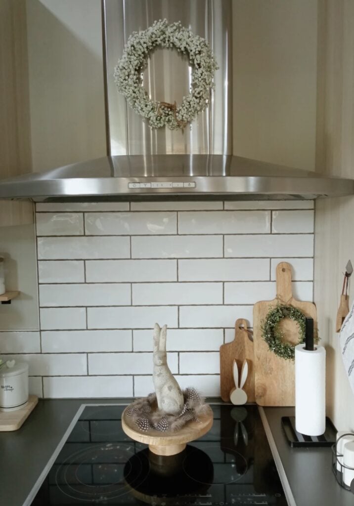 Minimal Easter kitchen decor with a bunny wreath above the stove, wood cutting boards, a small bunny silhouette, and a neutral bunny centerpiece on a pedestal stand.