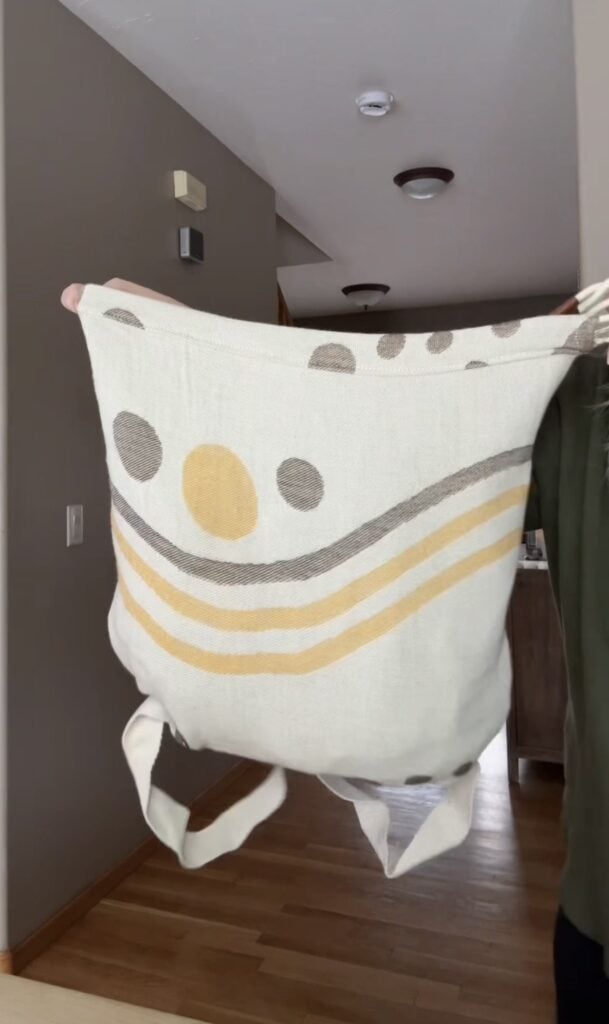 Sand Cloud towel backpack folded into backpack form showing cream and gold striped design with backpack straps hanging down