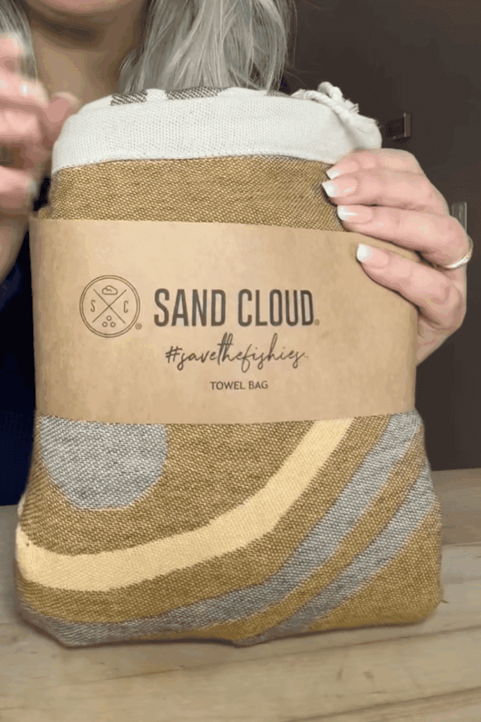 Sand Cloud towel backpack in original kraft paper packaging band showing brand name
