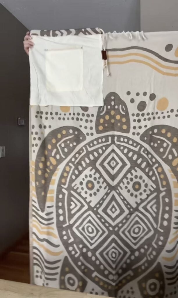 Sand Cloud towel backpack laid flat showing full size mudcloth turtle design in cream and gold with built-in zipper pouch visible in corner