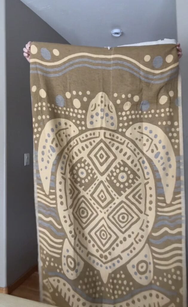 Sand Cloud towel backpack unfolded to full size showing mudcloth turtle design in tan and cream with geometric patterns