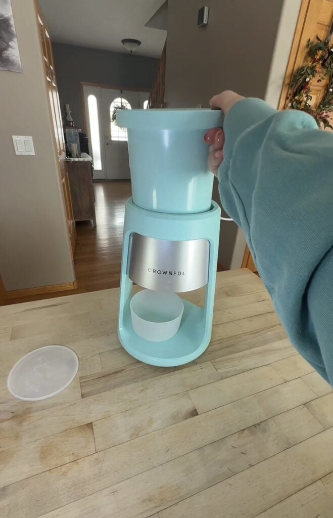 Crownful shave ice machine with frozen ice cup being placed into the top on a kitchen table.