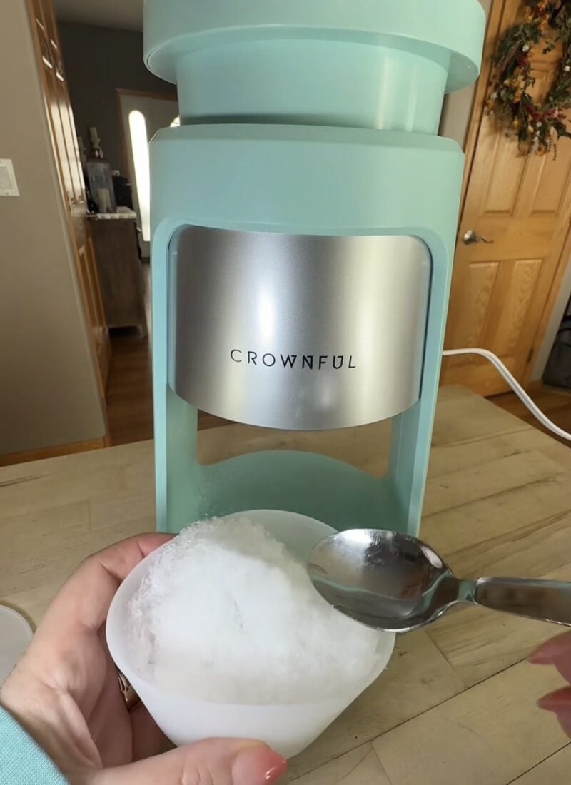 Freshly shaved ice in the small cup in front of the Crownful machine with a spoon ready to use.