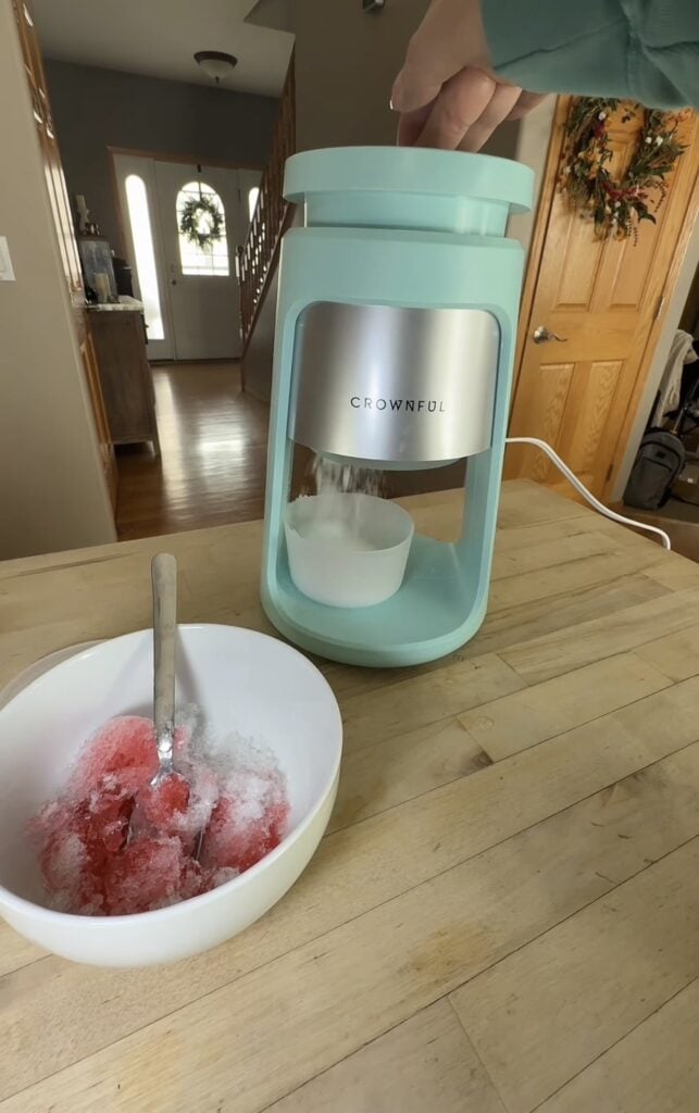 Red shaved ice snow cone in a white bowl beside the Crownful machine.