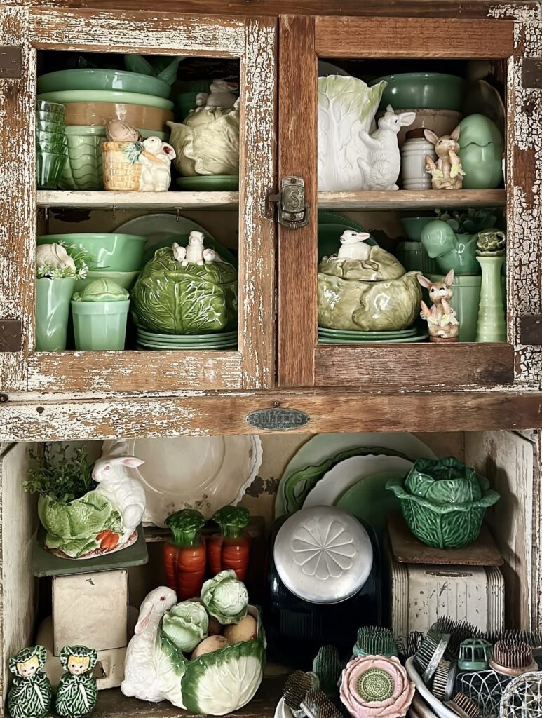 Vintage Easter kitchen hutch decor with green cabbage dishware, ceramic rabbits, pastel egg accents, and rustic distressed wood cabinet styling.