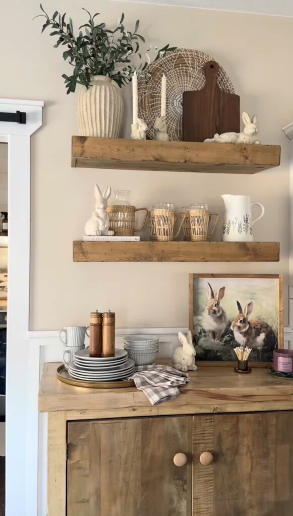 Neutral Easter shelf decor with wooden floating shelves, wicker chargers, ceramic bunnies, framed rabbit art, stacked dishes, and soft farmhouse spring accents.