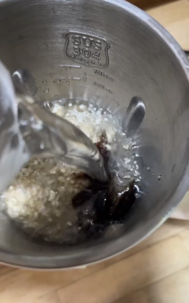 Water being poured over oats and dates inside the stainless steel Iagreea oat and nut milk maker machine, featured on slowestuff.com.
