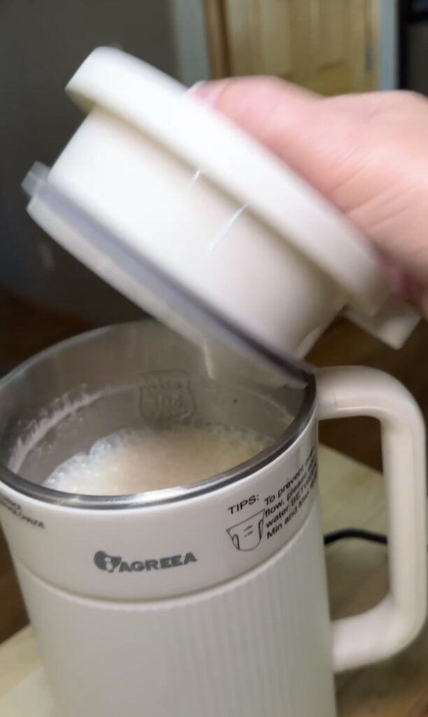 Top view of the white Iagreea nut milk maker machine with the lid lifted to show frothy homemade plant milk inside, featured on slowestuff.com.