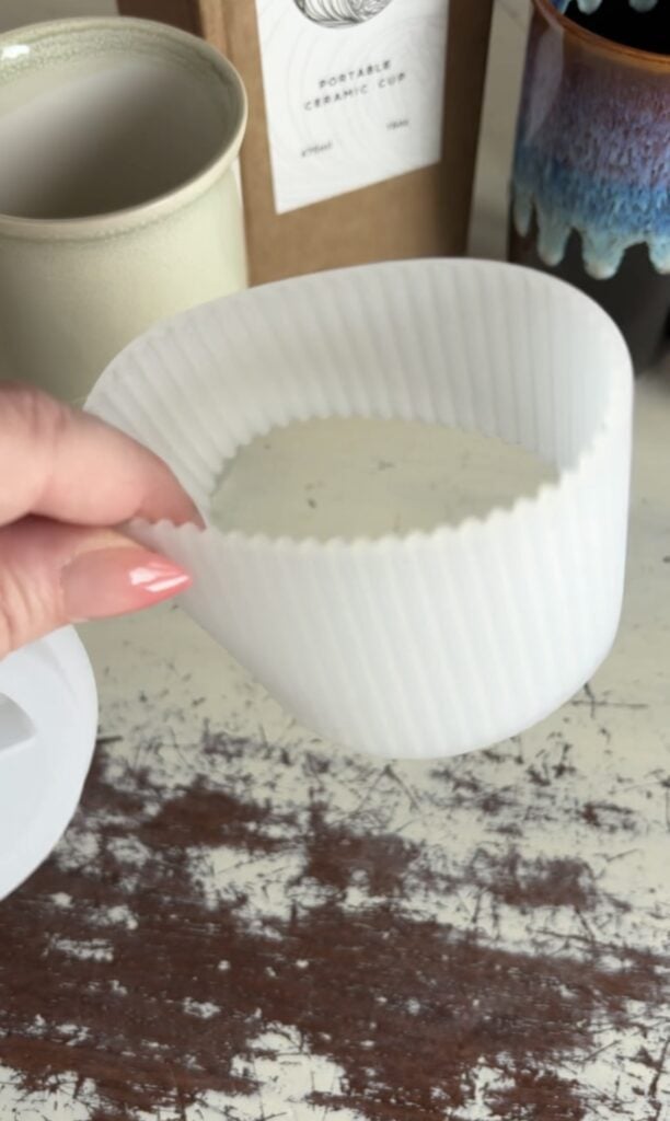 White ribbed silicone sleeve accessory for a Nova Ceramics travel mug being held in front of the mugs and product packaging.