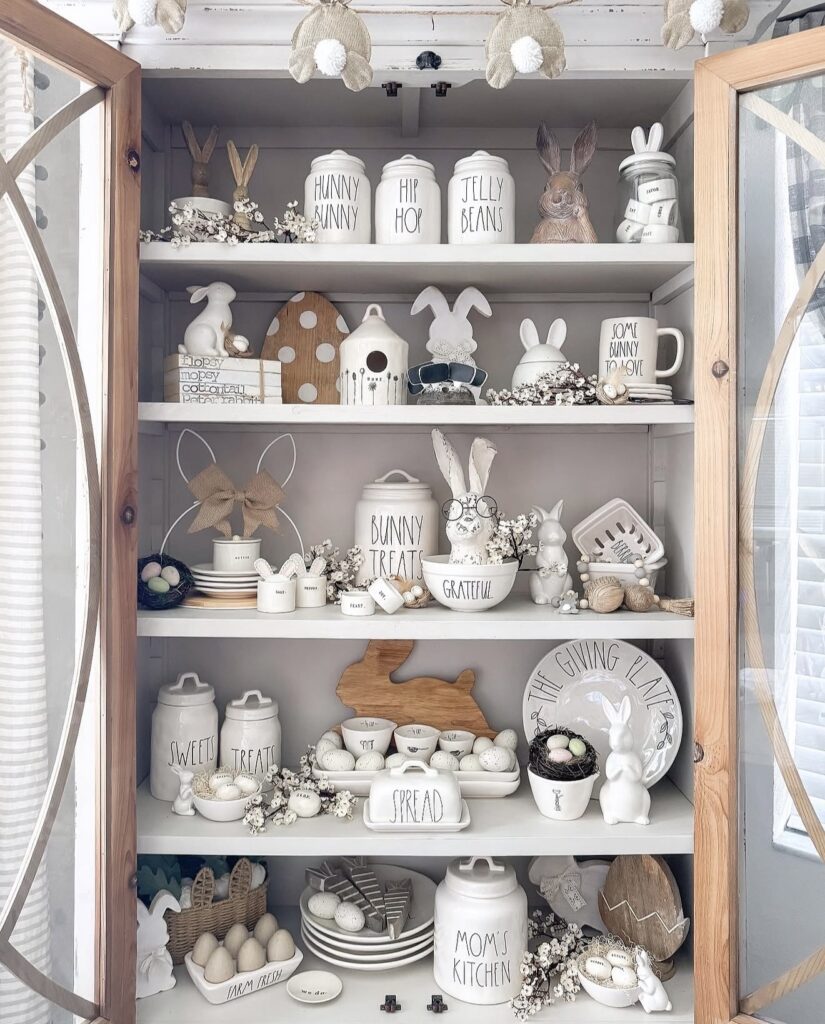 Rae Dunn Easter kitchen hutch decor with bunny canisters, egg accents, white ceramic serving pieces, wooden bunny shapes, and spring shelf styling.