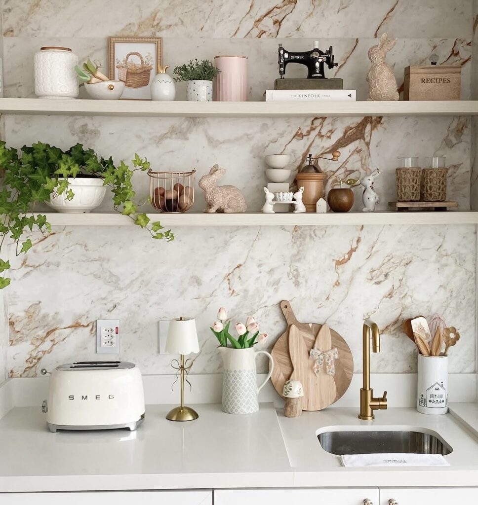 Classic Easter kitchen shelf decor with marble-look backsplash, bunny figurines, pink tulips, trailing ivy, egg accents, and soft neutral styling above the counter.
