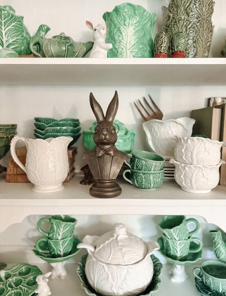 Green-themed Easter kitchen shelf decor with cabbage dishware, ceramic rabbit figurines, carrot accents, and rustic spring styling in a distressed wood cabinet.