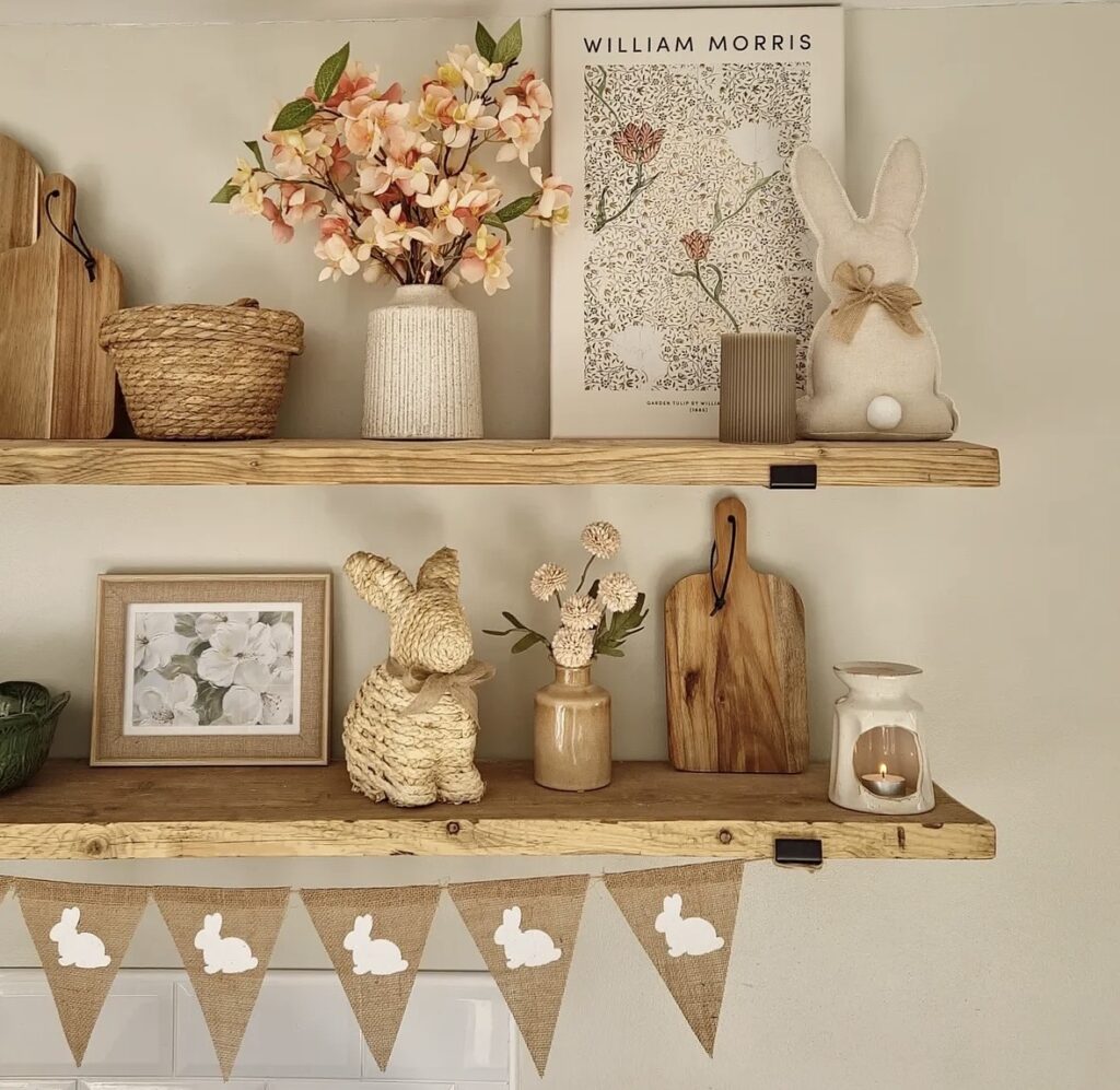 Natural Easter kitchen shelf decor with wicker baskets, blush florals, bunny figurines, wood cutting boards, bunny bunting, and warm neutral spring styling.