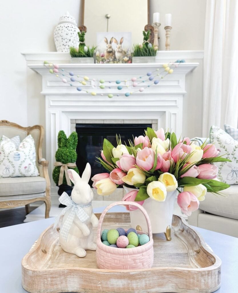 Classic Easter mantel decor with white bunny figurines, floral stems, neutral eggs, and layered spring accessories in a bright living room.