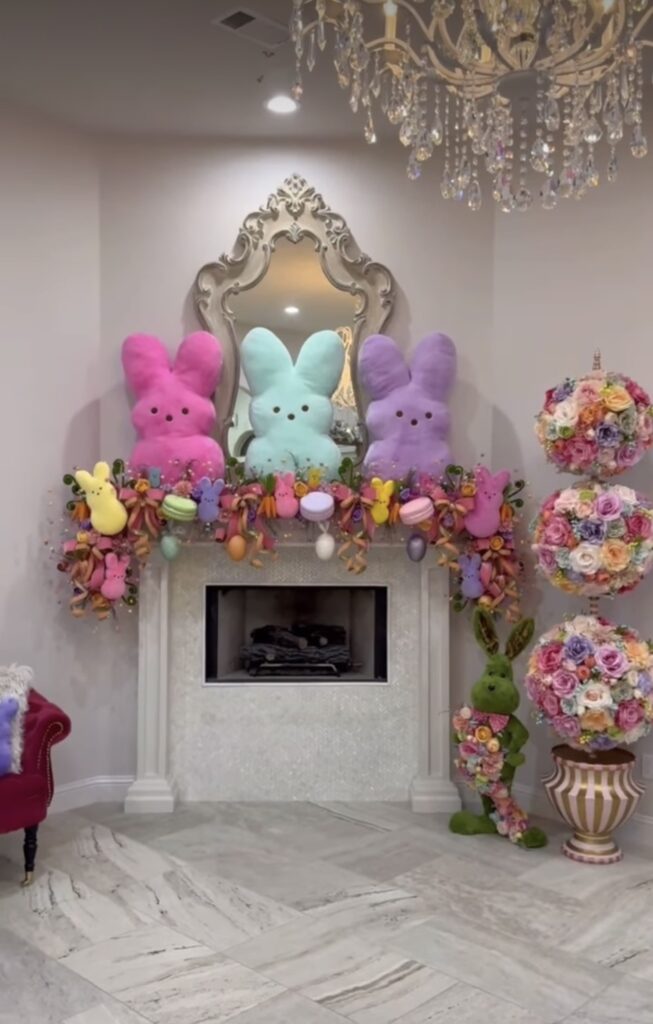 Classic Easter mantel decor with white bunny figurines, floral stems, neutral eggs, and layered spring accessories in a bright living room.