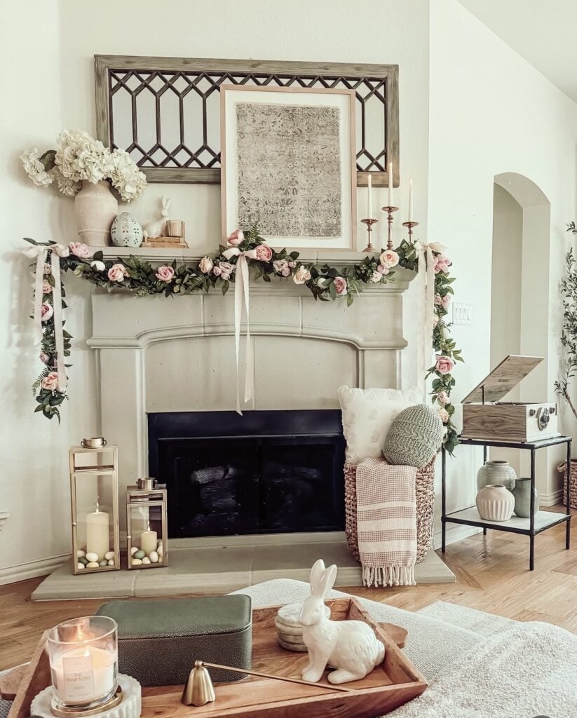 Elegant Easter mantel decor with woven bunny figurines, tulips, candles, and soft rose garland in a bright neutral living room.