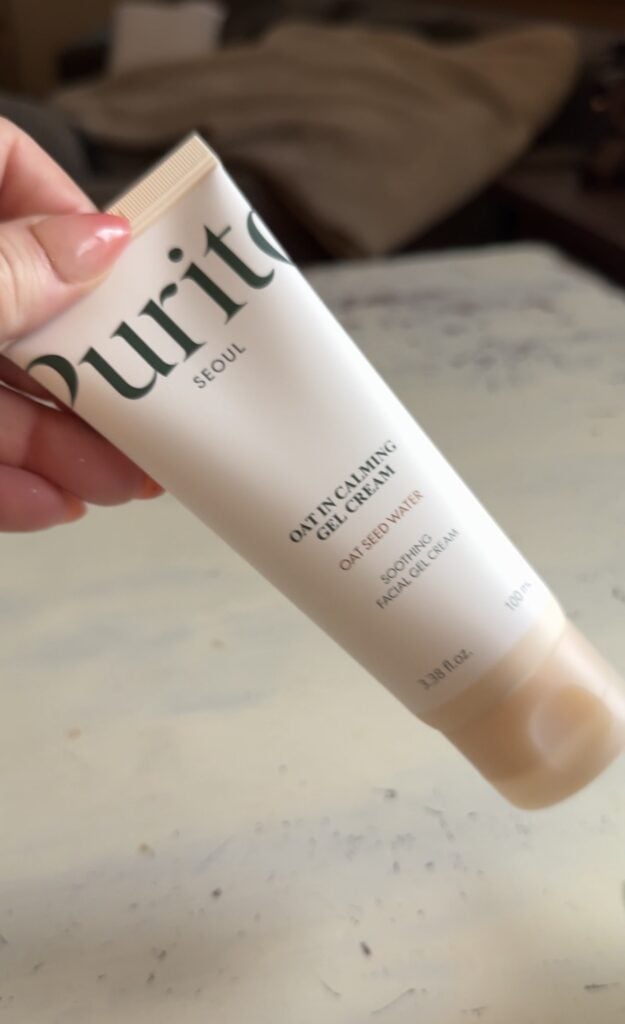 Hand holding Purito Seoul Oat In Calming Gel Cream with oat seed water on a soft neutral background