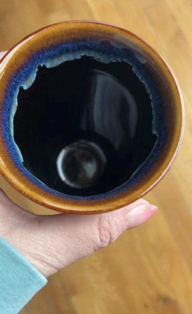 Top view inside a Nova Ceramics travel mug showing the glossy dark interior with a blue and amber glazed rim.