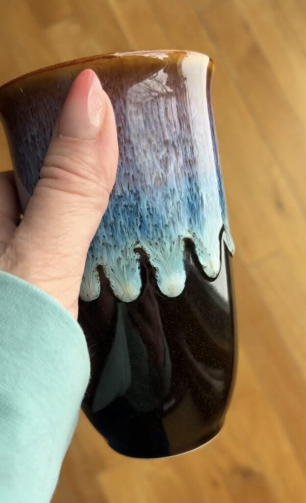 Close-up of a Nova Ceramics travel mug with a glossy black base and a flowing blue, aqua, and brown drip glaze design.