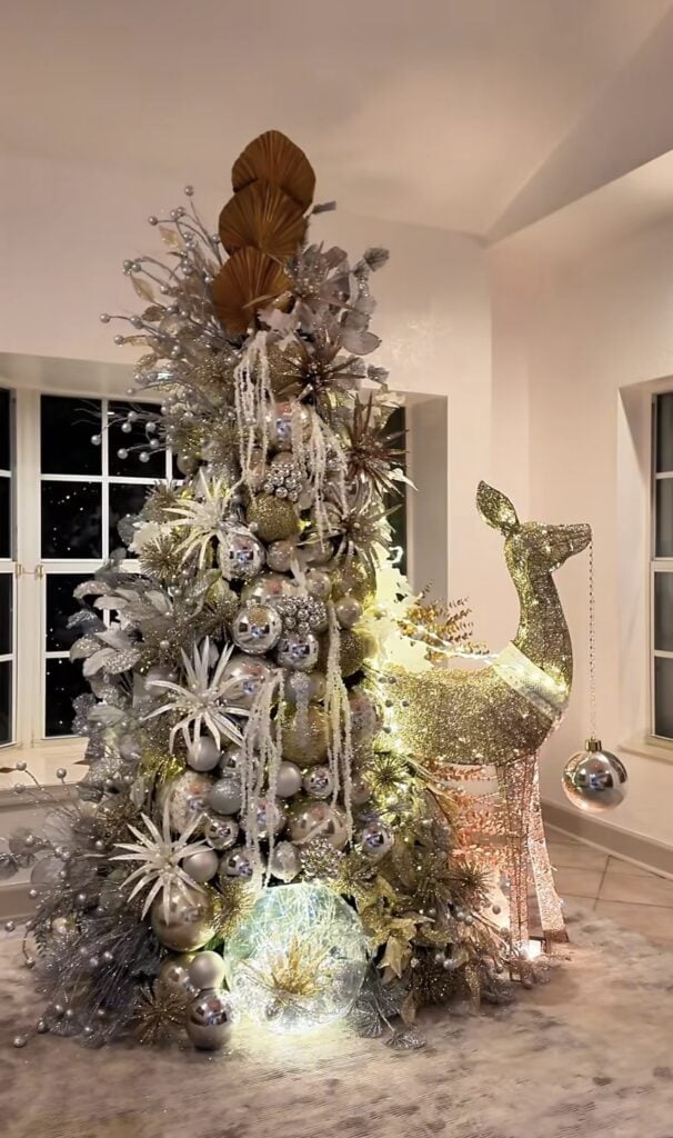 Whimsical gold Christmas tree with deer decorations, ribbon, and sparkling ornaments.