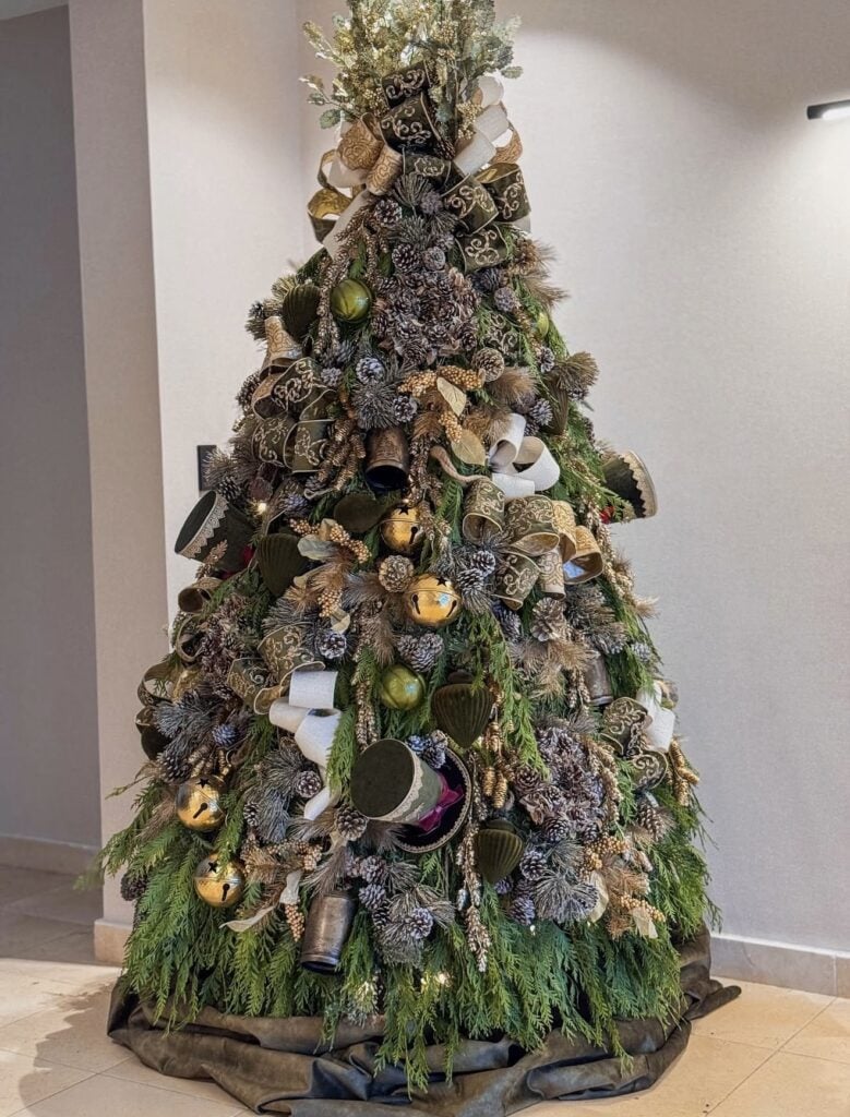 Nature-inspired Winter Solstice tree decorated with fresh evergreen branches, pinecones, woodland ribbons, bells, and natural textures in earthy green and gold.
