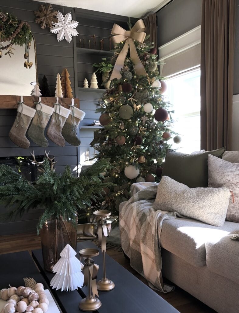 Dark brown Christmas tree coordinated with rich neutral holiday decor in an elegant living room with gold bow topper