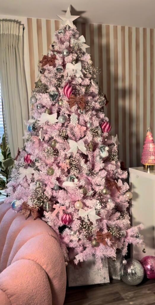 Pink artificial Christmas tree decorated with white bows, silver and hot pink ornaments, rose gold accents, and a white star topper in a colorful modern living room.