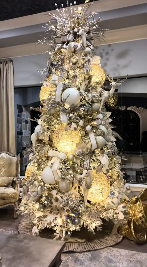 Gold Christmas tree decorated with lit up globe golden metallic ornaments, ribbon, and elegant holiday styling.