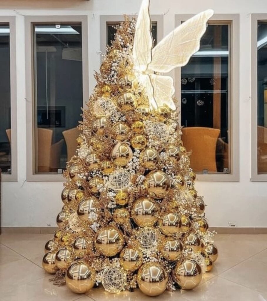 Gold Christmas tree with whimsical oversized butterfly  ornament, ribbon, and warm holiday lighting.