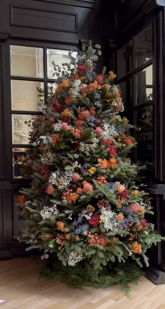 Nature-inspired Winter Solstice tree featuring flowers and greenery in outdoor patio setting.