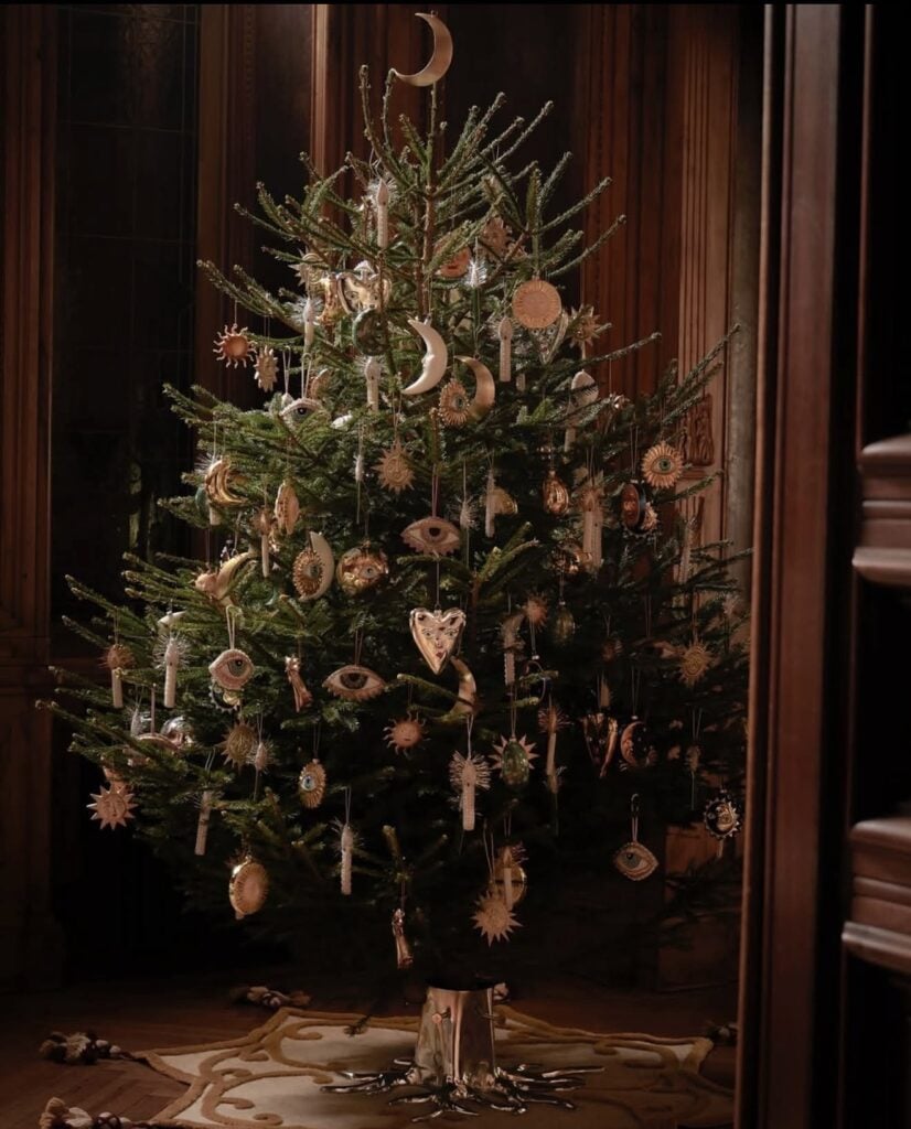 Celestial Winter Solstice tree decorated with moon, sun, and eye ornaments, candles, and gold accents on natural evergreen branches.