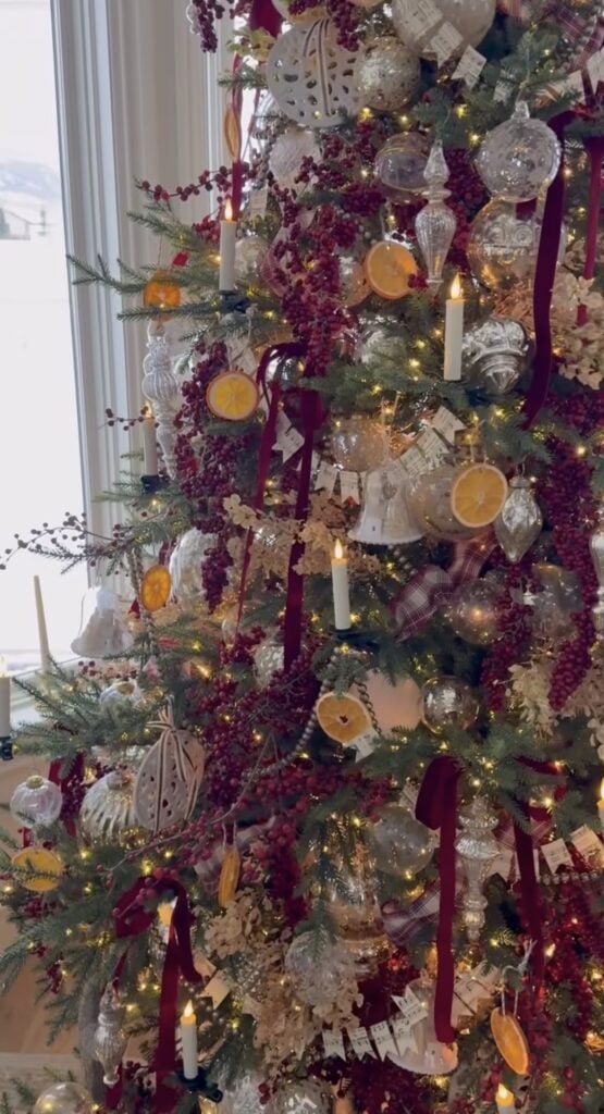 Elegant Winter Solstice tree decorated with earthy natural elements, clear ornaments, frosted ornaments, berries, evergreen branches, and warm lights with burgundy ribbon