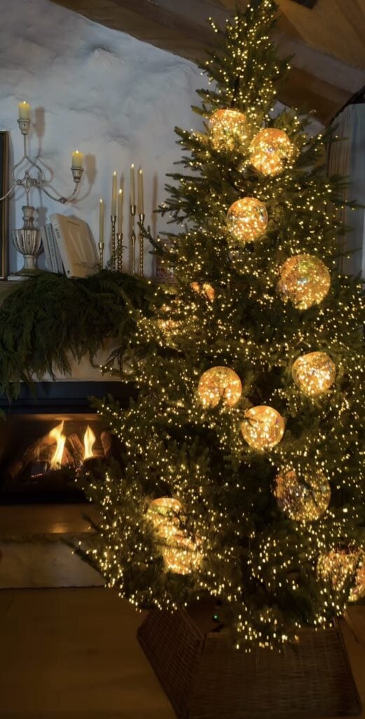 Elegant Winter Solstice tree decorated with warm fairy lights and oversized glowing glass globe ornaments beside a cozy fireplace.