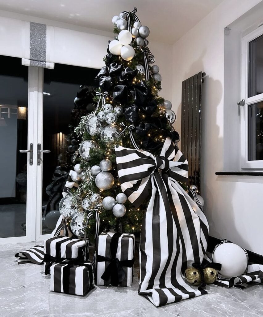 Black and white Christmas tree topped with an oversized striped bow and decorated with coordinating monochrome ornaments.