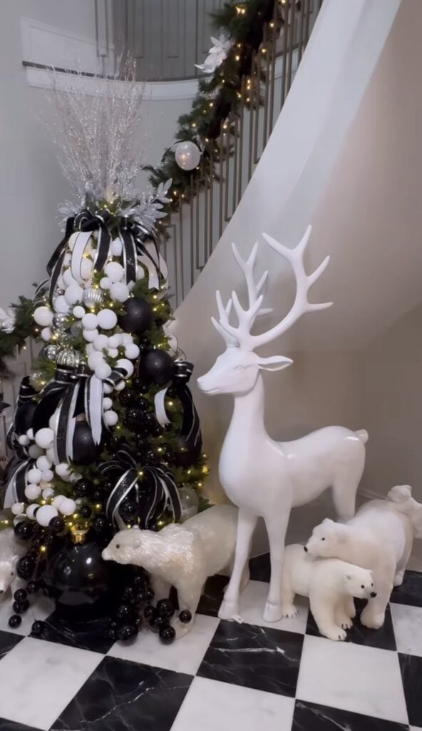 Black and white Christmas tree glowing with warm white lights and layered monochrome holiday decorations.