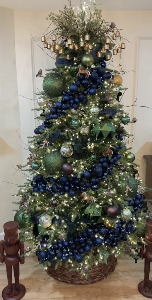 Blue and green Christmas tree styled with brass bells, velvet ribbon, natural greenery, and warm white lights.