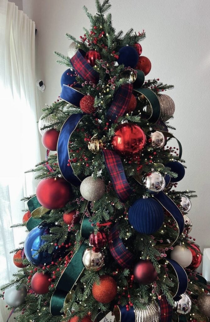 Traditional Christmas tree decorated with navy blue, red, plaid ribbon, classic ornaments, and warm lights for a collected holiday look.