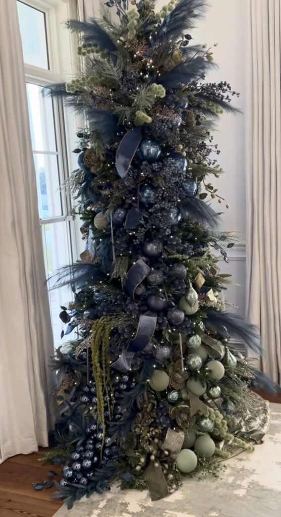 Christmas tree decorated with blue and sage green ornaments, soft ribbon, natural greenery, and warm holiday lights.