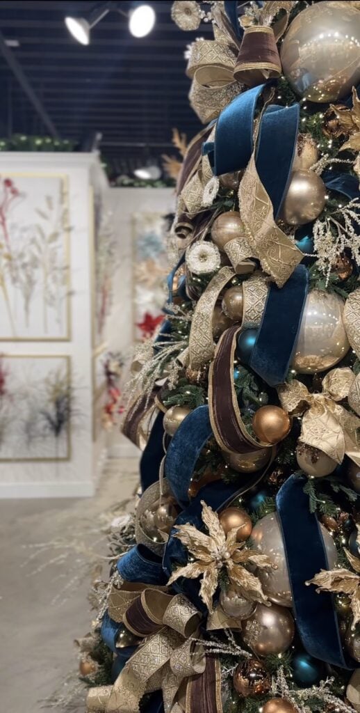 Close-up of a glamorous blue Christmas tree with layered blue ornaments, metallic accents, ribbon, and sparkling holiday details.
