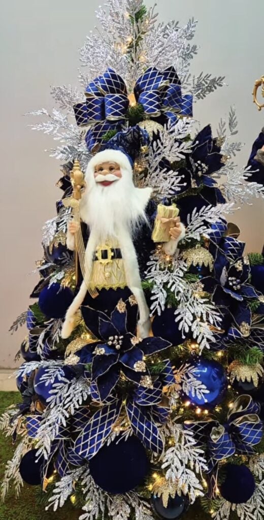 Blue Christmas tree featuring an oversized Santa decoration, blue ornaments, festive ribbon, and playful holiday accents.