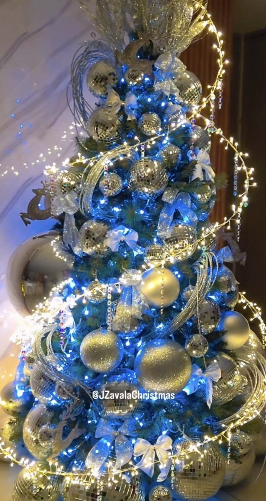 Blue Christmas tree decorated with swirl lights and blue lights, metallic ornaments, sparkling accents, and warm white lights.