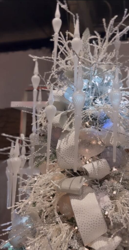 White Christmas tree illuminated with blue lights and decorated with white ornaments, icy accents, and shimmering winter details.