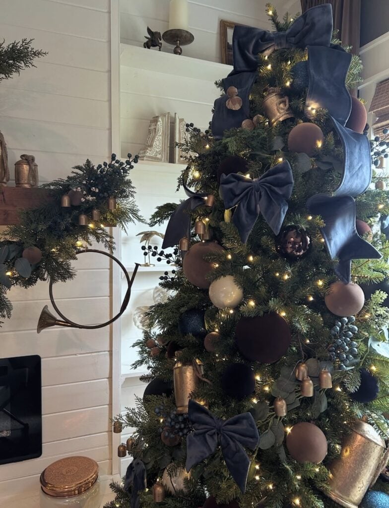 Christmas tree styled with layered blue ornaments, coordinating ribbon, metallic details, and warm white lights.