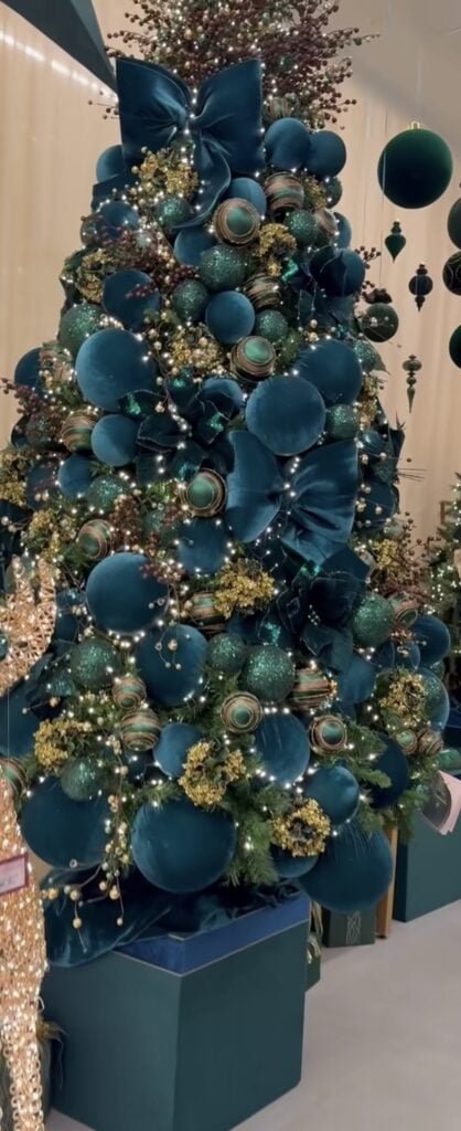 Christmas tree decorated with blue and teal ornaments, coordinating ribbon, metallic accents, and glowing holiday lights.