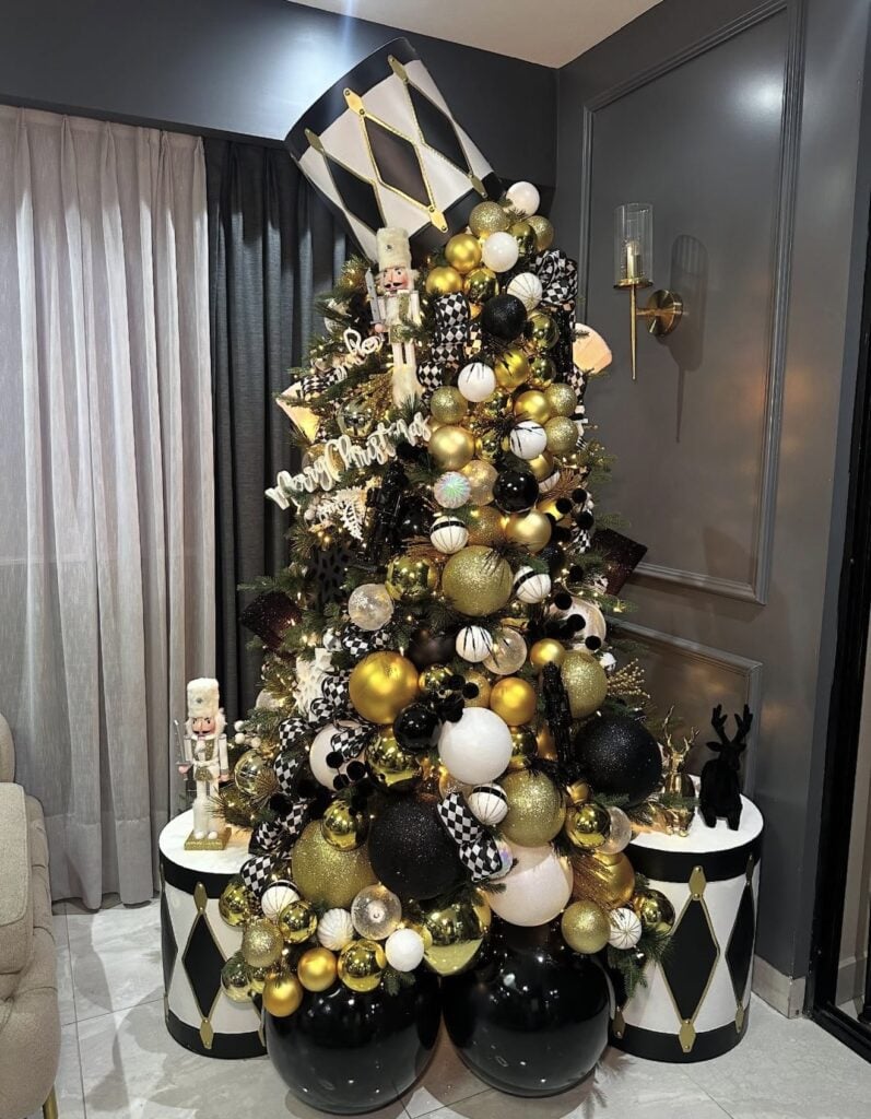Christmas tree decorated in black, white, and gold with harlequin patterns, metallic ornaments, and bold holiday accents.